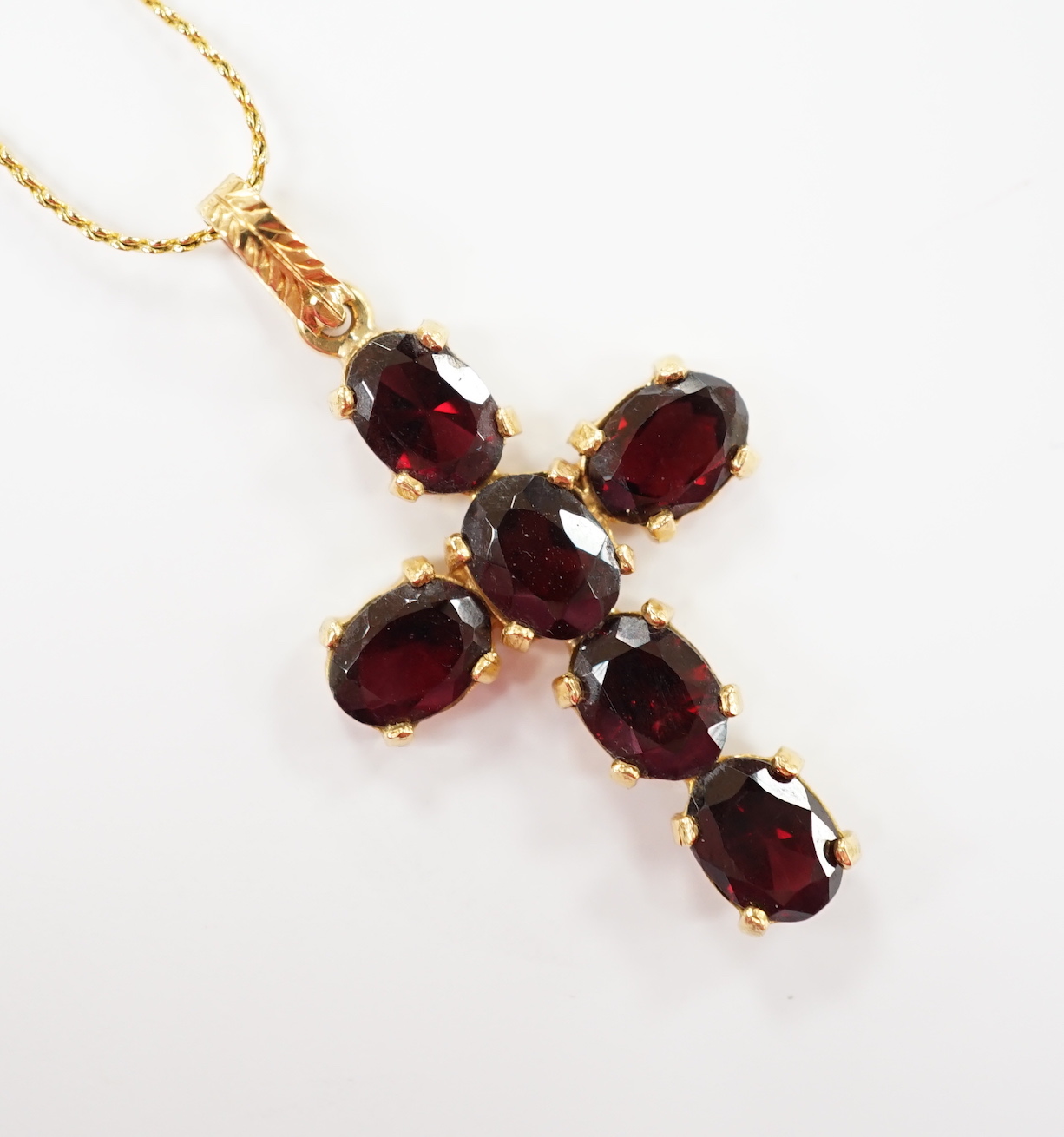 A modern 750 yellow metal and six stone oval cut garnet set cross pendant, 38mm, gross weight 3.5 grams, on a gilt metal chain.